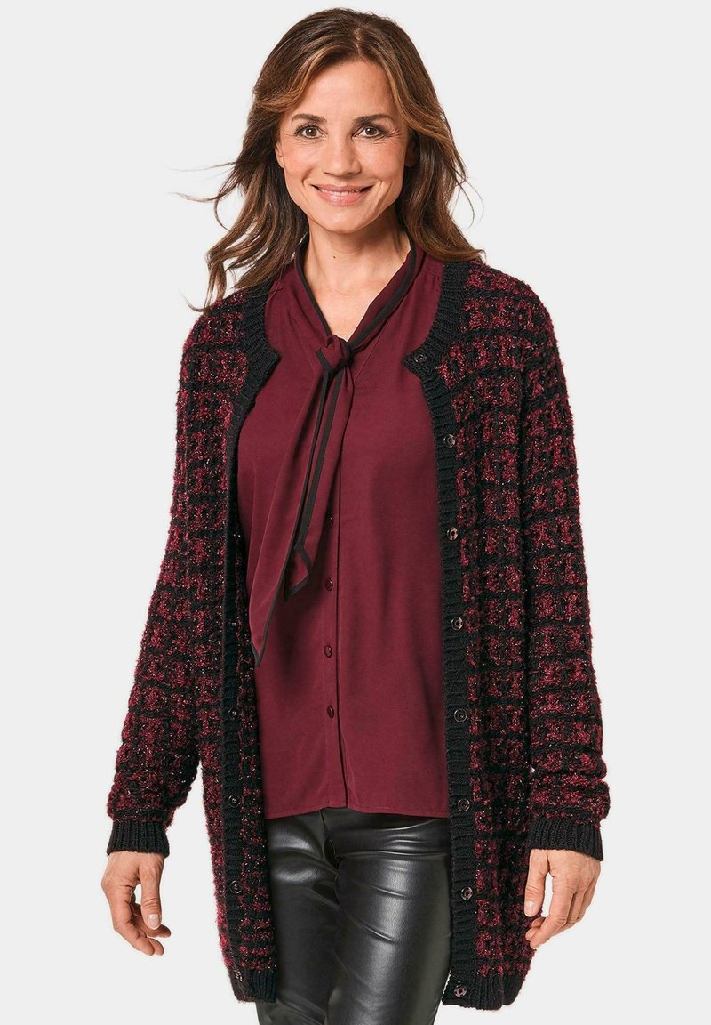 Langer Cardigan aus burgunderfarbenem und schwarzem strukturiertem Strick, mit Knopfverschluss und gerippten Bündchen, über einem burgunderfarbenen Top mit Schleifendetail getragen.