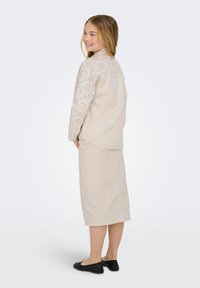 Bežinė medvilninė apranga, turinti trumpas rankoves su perforuotais gėlių akcentais, derinama su iki kelių siekiančia sijonu ir juodais batais.