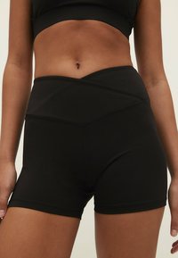 Zwarte high-waisted sportshorts met een gladde textuur, voorzien van een schuine tailleband en naadloos ontwerp. Geschikt voor actieve kleding.