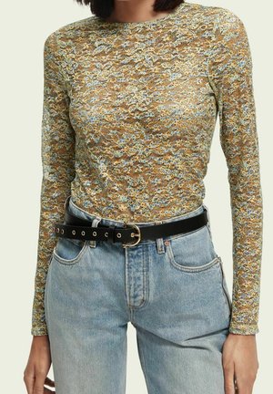 Femme portant un haut à manches longues à motif floral, rentré dans un jean taille haute bleu clair avec une ceinture noire.