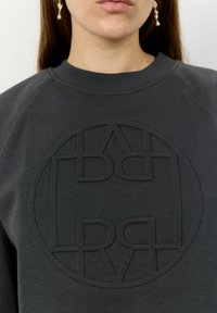 Sweatshirt gris foncé avec un logo texturé comportant des lettres entrelacées, col rond et poignets côtelés. Tissu doux, design décontracté.