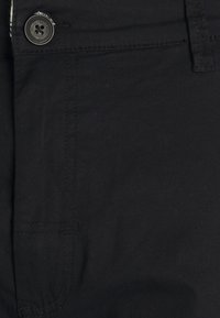 Tejido negro con un acabado suave, con un cierre de botones en la parte delantera y detalles de costura sutiles, que muestra un diseño clásico de pantalón.
