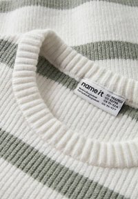 Pull en maille côtelée avec des rayures blanches et vert clair. Il présente un col rond large et une étiquette en tissu indiquant la taille et les instructions d'entretien.