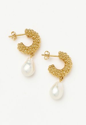 Złote kolczyki koła o teksturowanej powierzchni z nieregularnymi białymi perłowymi zawieszkami, z zapięciem na sztyft, na białym tle.