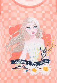 Pinkes Tanktop mit einem grafischen Design eines Charakters mit langen blonden Haaren, umgeben von Blumen und einem Text, der sagt: "Feiere die Saison."