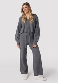 Felpa grigia corta con maniche ampie, abbinate a pantaloni larghi coordinati. Entrambi sono realizzati in tessuto morbido. Il modello indossa sneaker bianche.