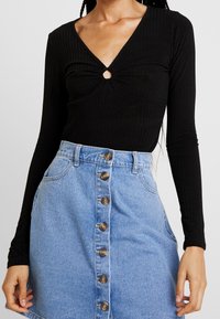 Svart ribbad långärmad topp med V-ringning och centralt nyckelhål, kombinerad med en ljusblå knäppning denimkjol.