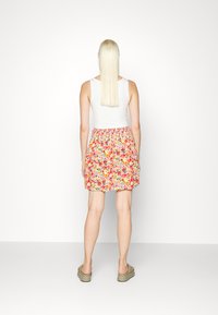 Saia de estampado floral com elástico na cintura, apresenta cores vibrantes como rosa, amarelo e verde. Combinada com uma t-shirt branca.
