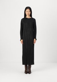 Μαύρο πλισέ maxi φόρεμα με μακριά μανίκια και στρογγυλή λαιμόκοψη, με υποτονική υφή. Φορεμένο με καφέ κομψά μποτάκια μέχρι τον αστράγαλο.