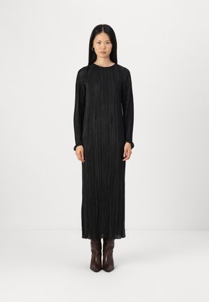 Black pleated maxi dress with long sleeves and rounded neckline, featuring subtle texture. Worn with brown pointed ankle boots.