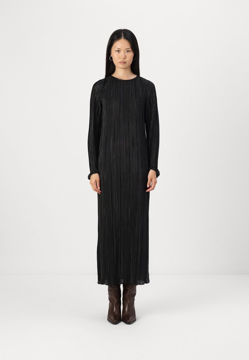 Μαύρο πλισέ maxi φόρεμα με μακριά μανίκια και στρογγυλή λαιμόκοψη, με υποτονική υφή. Φορεμένο με καφέ κομψά μποτάκια μέχρι τον αστράγαλο.