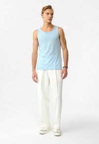 Lichtblauw tanktop met een geribbeld patroon, gecombineerd met losse, witte, textuurbroeken en witte sneakers met grijze accenten.