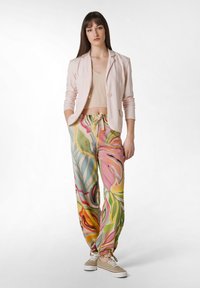 Ljusrosa blazer, ribbat beige crop top och byxor med en flerfärgad blommönstring och elastiska muddar. Beiga sneakers fulländar outfiten.