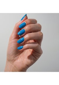 Un vernis à ongles bleu ciel recouvre des ongles longs et en forme d'oval. La main a un teint clair et est positionnée contre un fond clair.