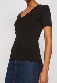 Svart V-ringad t-shirt i mjuk bomull. Fitted design med korta ärmar, med en liten logotyp på bröstet. Slät textur.