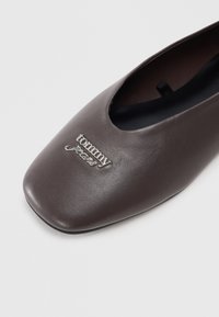 Dark brown square-toe flat shoe with black interior and metallic "tommy jeans" logo on the front upper part.