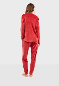 Ensemble de pyjama en velours rouge comprenant un haut à manches longues et un pantalon fuselé, orné de petits points dorés dispersés pour le détail et la texture.