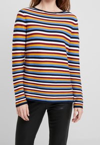 Haut à manches longues rayé avec des bandes horizontales rouges, jaunes, bleues et blanches, en tissu côtelé avec un col rond et des manches ajustées.