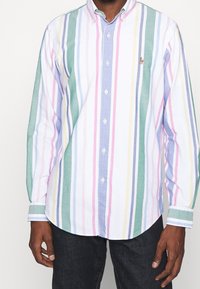 Camicia button-up con righe verticali in verde, blu, rosa e bianco. Presenta un colletto e maniche lunghe. Logo discreto sul petto.