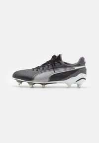 Botín de fútbol negro y plateado con un upper texturizado, cierre de cordones y tacos moldeados para tracción. Presenta un logo sutil en el talón.