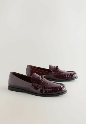 Burgundowe lakierowane mokasyny z gładkim wykończeniem, z ozdobnym szyciem i małym kokardowym detalem na cholewce. Czarna gumowa podeszwa.