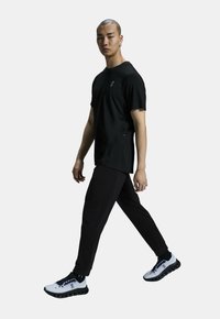 T-shirt de sport noir à manches courtes, associé à un pantalon noir ajusté et des chaussures de course blanches avec des semelles noires et des accents bleus.