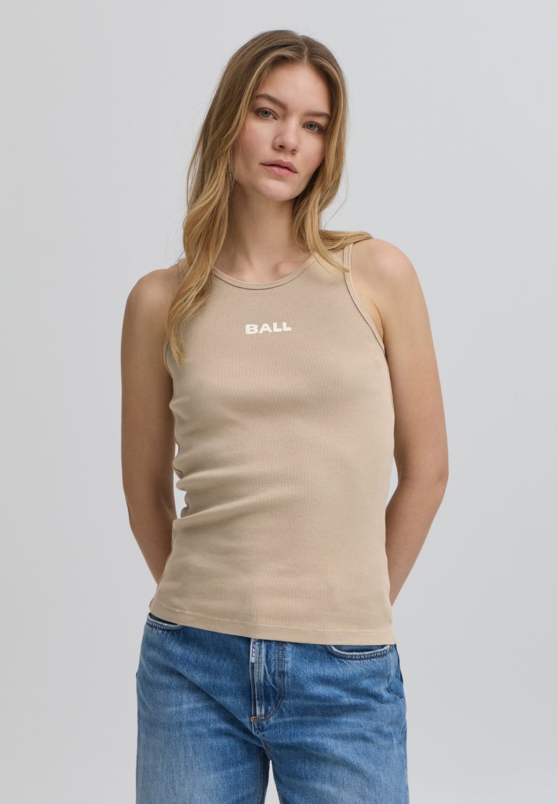 Beige gerippter Tanktop mit rundem Ausschnitt, auf dem die weiße Aufschrift "BALL" über der Brust prangt. Kombiniert mit blauen Jeans.