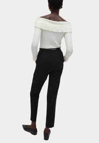 Witte off-shoulder textuurtop, zwarte tapered broeken en zwarte platte schoenen, gezien vanachter met een elastische taille_detail.