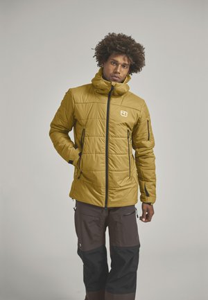 Yellow insulated jacket with a high collar, featuring quilted design, two side pockets, and a logo on the chest. Brown and black trousers.