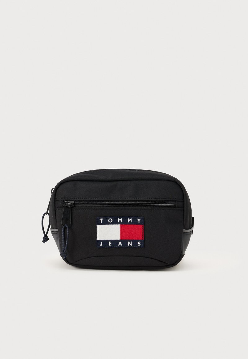 Sort stof talje taske med en frontlynlås, der har et flerfarvet broderet logo-patch med røde, hvide og blå rektangler.