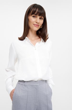 White long-sleeve shirt with a collar and buttoned front, paired with light gray, tailored trousers featuring side pockets and a smooth texture.
