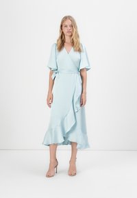 Vestido envolvente azul claro com mangas soltas e bainha com babados, feito de um tecido suave. Apresenta um fecho com laço na cintura.