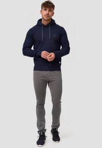 Námořnická mikina s kapucí z texturované látky, šedé šňůrky a logo na hrudi; v kombinaci s šedými kalhotami slim fit a černými teniskami.