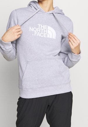 Osoba nosząca jasnoszary kaptur The North Face trzymająca troczki, w parze z luźnymi czarnymi spodniami.