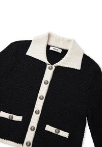 Schwarzer strukturierter Cardigan mit einem cremefarbenen gerippten Kragen, der eine Knopfleiste und zwei aufgesetzte Taschen hat. Silberfarbene Knöpfe setzen Akzente.