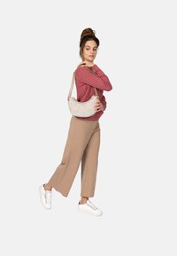 Beige Handtasche mit Kettenriemen, strukturiertes Frontmuster, kombiniert mit einem pinken Rippstrick-Pullover und beigen weiten Hosen, abgerundet mit weißen Sneakern.