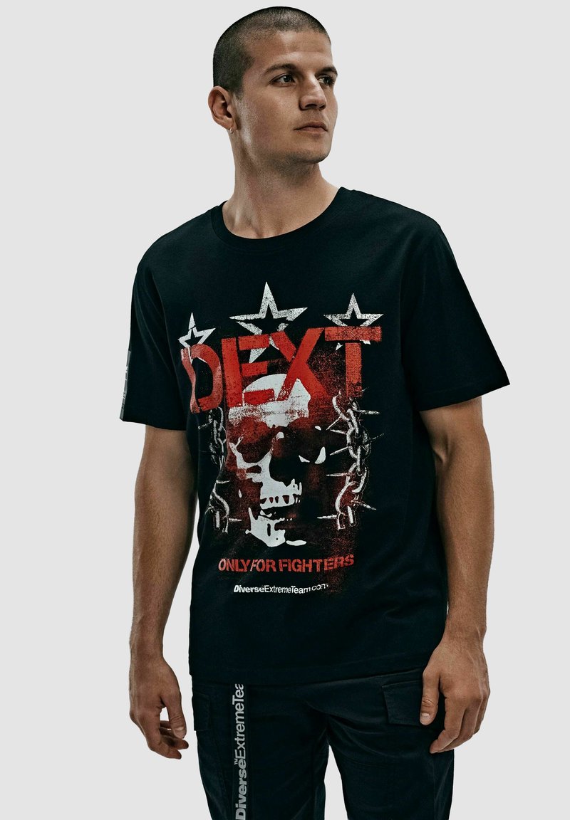 Czarny t-shirt z krótkim rękawem z graficznym wzorem przedstawiającym czaszkę, czerwonym i białym tekstem oraz akcentami w kształcie gwiazdek. Tkanina wydaje się gładka, w standardowym kroju.