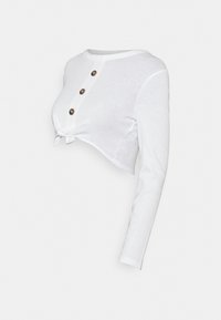 Vit långärmad croppad topp med tre bruna knappar framtill och en knutdetalj vid nederkanten.