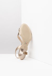Gold metallic strappy sandal with a square block heel, smooth texture, rubber sole, and printed brand details on the bottom. Size 37.