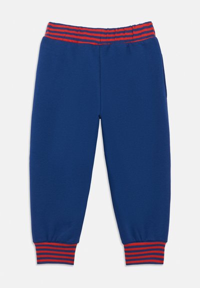 Calças de fato azuis com cintura e punhos elásticos em riscas vermelhas e azuis, apresentando bolsos laterais e um corte descontraído.