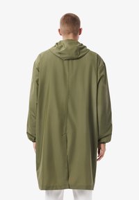 Impermeabile verde oliva con cappuccio, caratterizzato da una vestibilità lunga e ampia, polsini elasticizzati, texture liscia e un design semplice e minimalista.