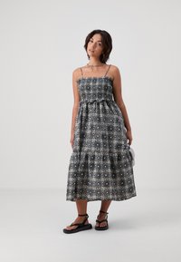 Čierno-biel dress so vzorom, tenkými ramienkami, smockovaným telom, vrstvenou sukňou a voľným strihom. Nosené s čiernymi sandálmi.