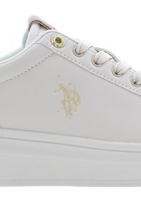 Bílé kožené tenisky se světle modrými akcenty, kulatými tkaničkami, zlatými kroužky na tkaničky a diskrétním zlatým logem zobrazujícím hráče polo na boku.