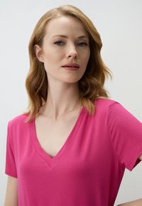 T-shirt rose à manches courtes avec un col en V. Fabriqué en tissu doux, il présente une texture lisse et une coupe décontractée.