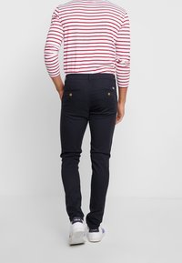 Granatowe spodnie slim-fit wykonane z mocnego materiału, z tylnymi kieszeniami i kontrastowymi, złotymi guzikami, połączone z koszulą w czerwono-białe paski.