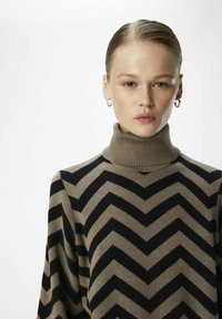 Maglione a collo alto a base di un morbido tessuto a maglia, con motivo a zig-zag marrone e nero, caratterizzato da un colletto a coste e una vestibilità rilassata.