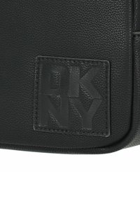 Borsa in pelle sintetica nera con superficie testurizzata, patch con logo DKNY in rilievo e dettagli cuciti. Design rettangolare semplice.