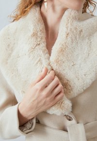 Beige wool coat with a soft, faux fur collar in light cream. The collar features a plush texture; closed with clear buttons and fabric belt.