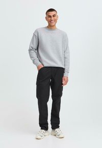 Gray sweatshirt with ribbed cuffs, paired with black cargo pants featuring side pockets. Model wears white sneakers. Simple, casual look.
