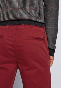 Czerwone bawełniane spodnie o gładkiej fakturze, z dwoma tylnymi kieszeniami i dopasowaną talią, połączone z czarnym i szarym swetrem w teksturowany wzór.